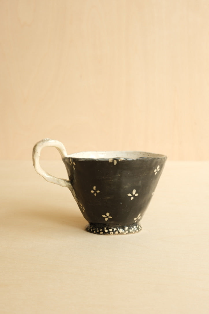 Black ceramic cup with floral patterns on a beige background
