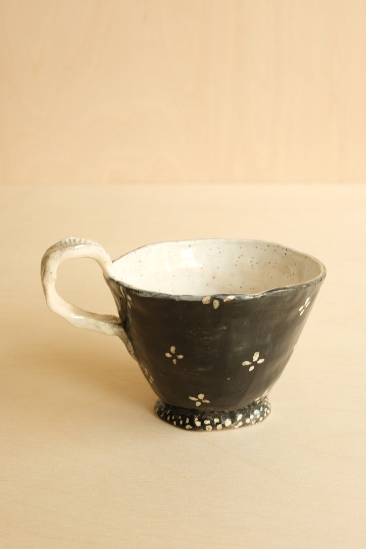 Black ceramic cup with white speckles on a beige background