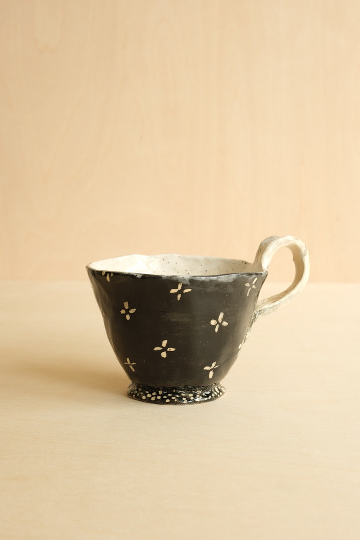 Black ceramic cup with white floral patterns on a beige background